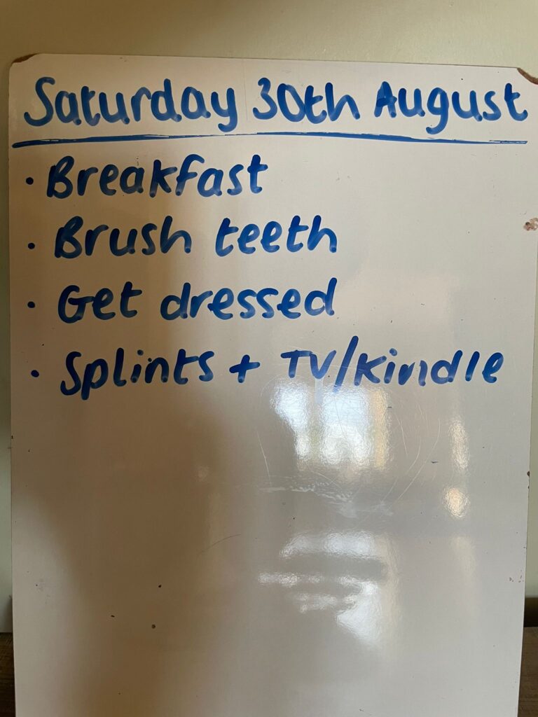 Whiteboard headed “Saturday 30th August” with a bulleted list: Breakfast; Brush teeth; Get dressed; Splints + TV/Kindle.