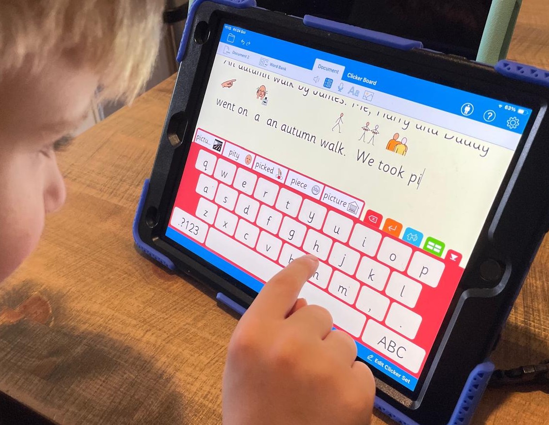 A child uses the on-screen keyboard in Clicker Writer on an iPad to type a sentence with symbol support about an autumn walk.
